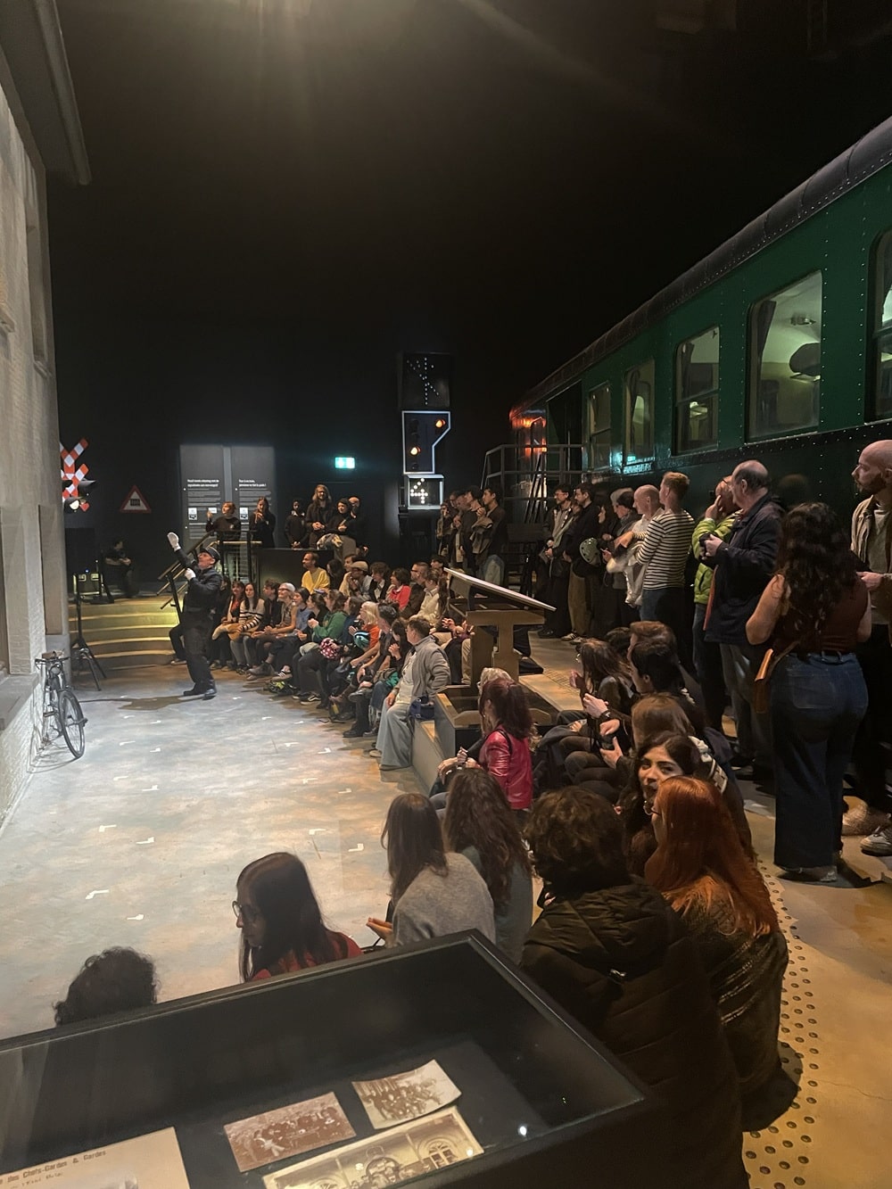 Publiek bij Museum Night Fever, zittend rond een podium met een treinwagon op de achtergrond.