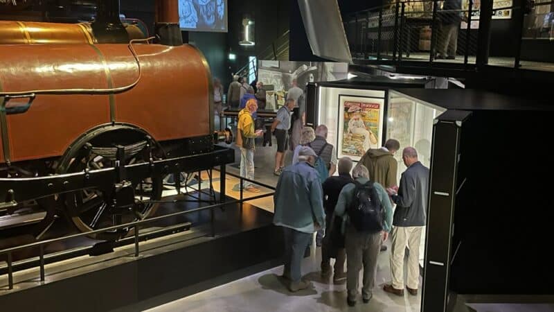 Bezoekers bekijken een antieke stoomlocomotief in een museum, met mode-elementen.