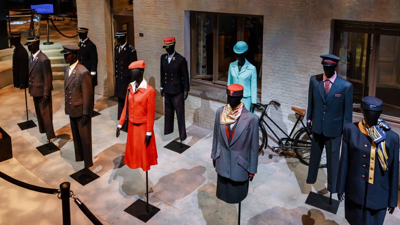 Mannequins display vintage uniforms, including a bright orange suit and navy blue attire.